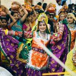 A group of traditionally dressed Indian women perform a vibrant folk dance in a crowded outdoor celebration in Nagaur Cattle Fair festival 2026 while a man plays a drum.